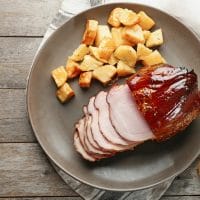 A platter with maple glazed ham and roasted potatoes.