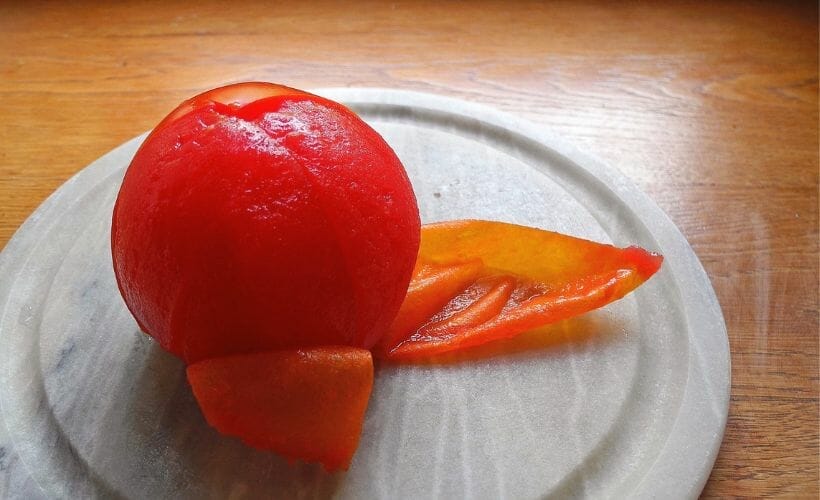 A picture of a peeled tomato sitting on a marble coaster on a wooden table.