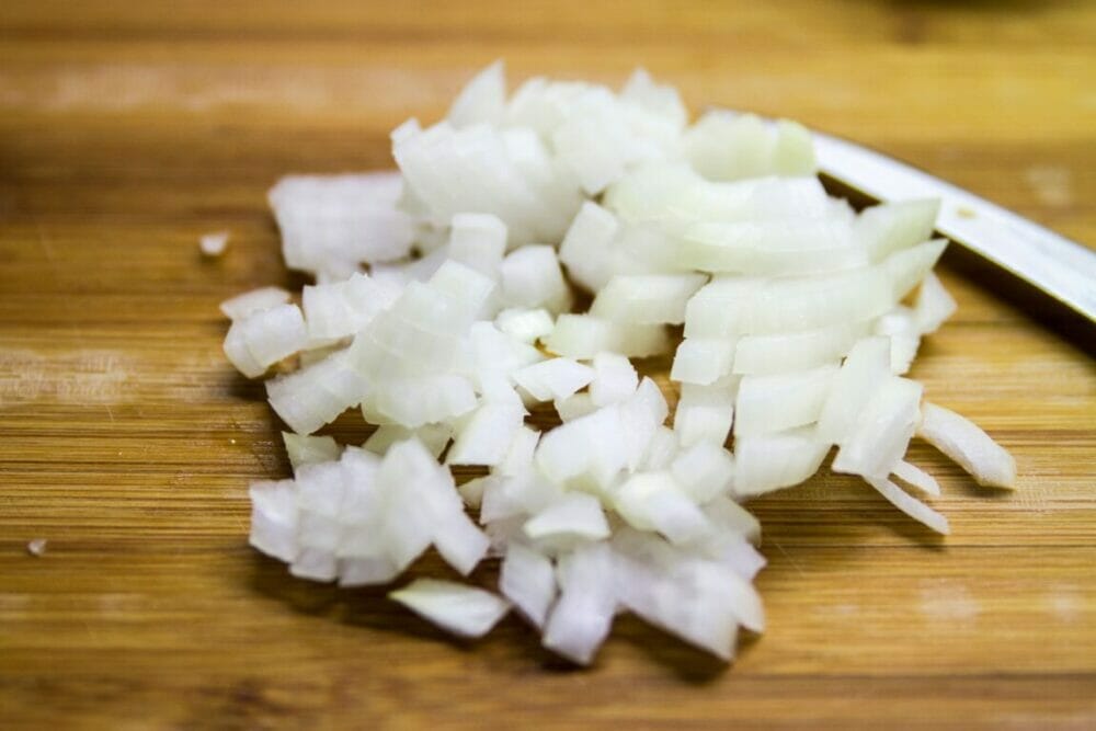 Coarsely chopped white onion on a bamboo cutting board.