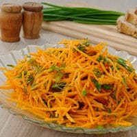 Carrot salad in a large glass serving bowl and topped with fresh parsley.