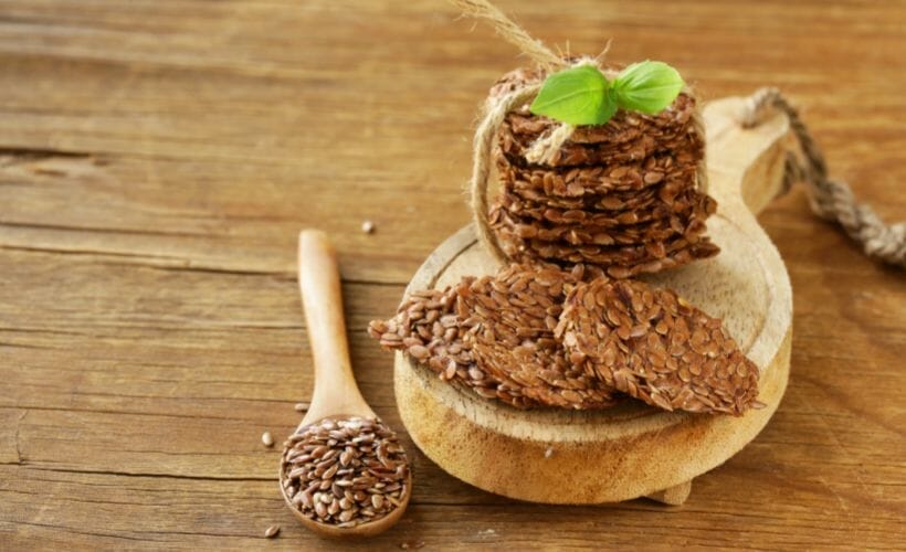 Raw flax seed crackers in a stack and tied up with twine and a spoon of flax seeds.
