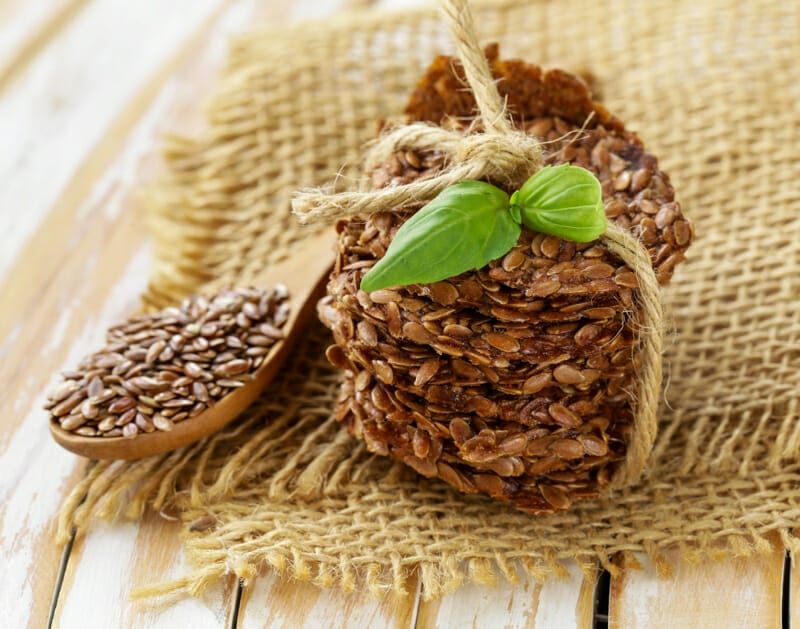 A stack of raw flax seed crackers on burlap with a spoon of flax seeds.
