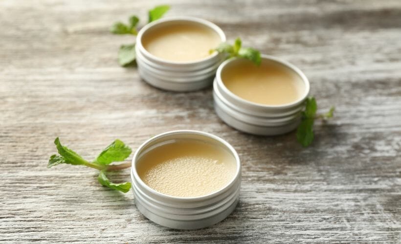 Three jars of salve in small tins laying out on a table with sprigs of mint.
