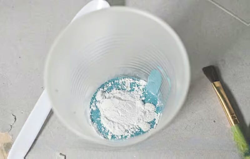 Adding grout to a plastic cup of blue acrylic paint.
