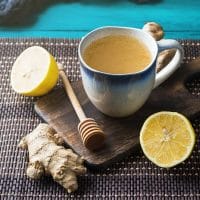 A blue and white cup of pain-relieving herbal tea with lemon halves and a piece of ginger root.