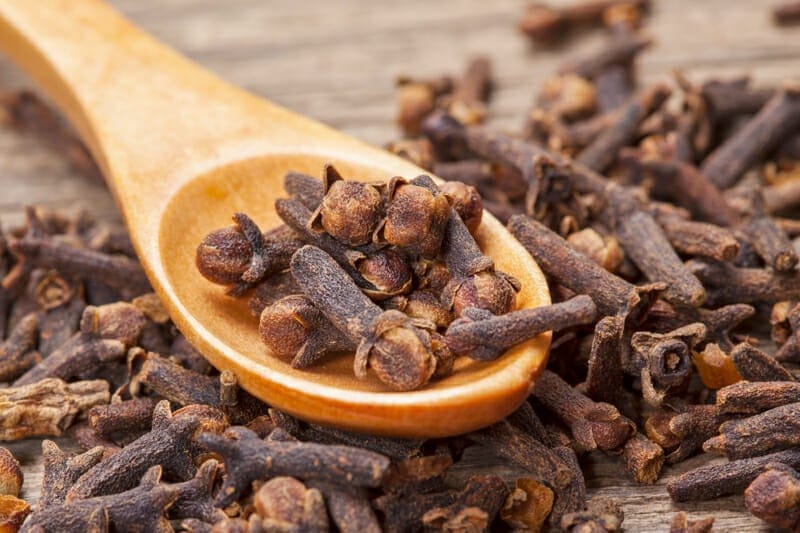 A spoonful of dried cloves on a cutting board.