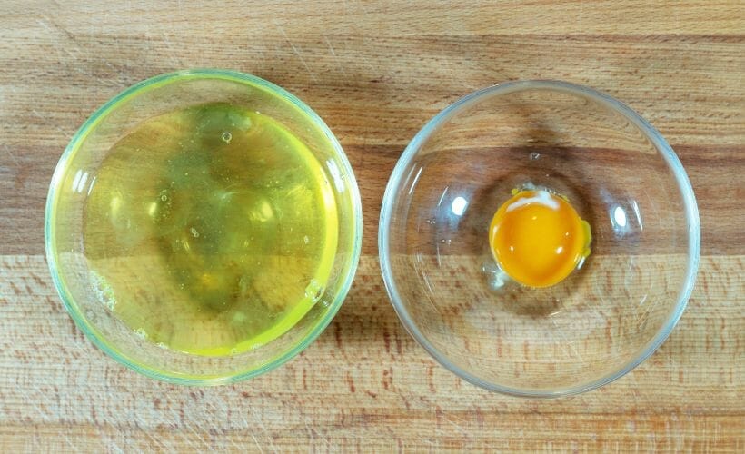 A clear bowl of egg whites next to a clear bowl with an egg white.