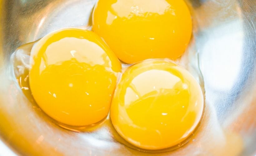 Three egg yolks in a metal bowl.