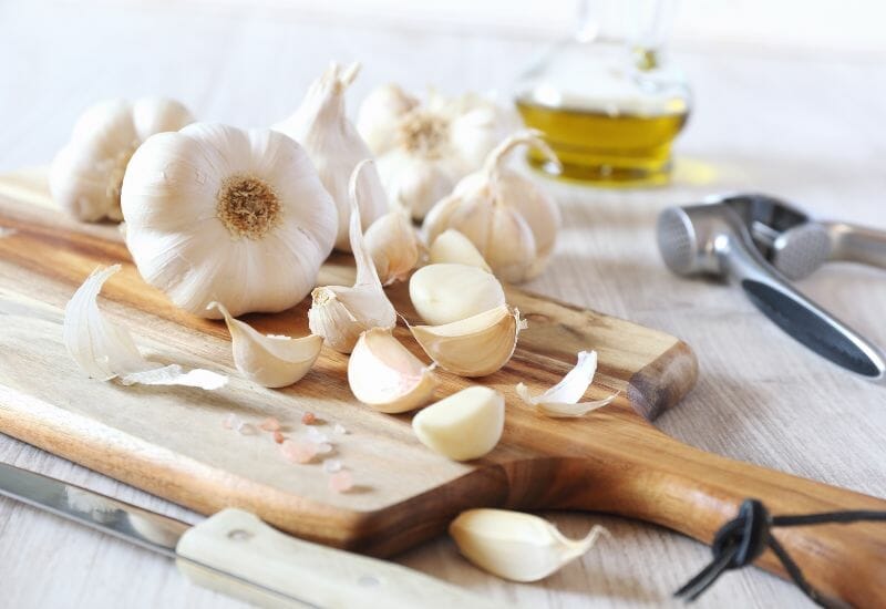 A head of garlic broken down into cloves with a jar of oil in the background.