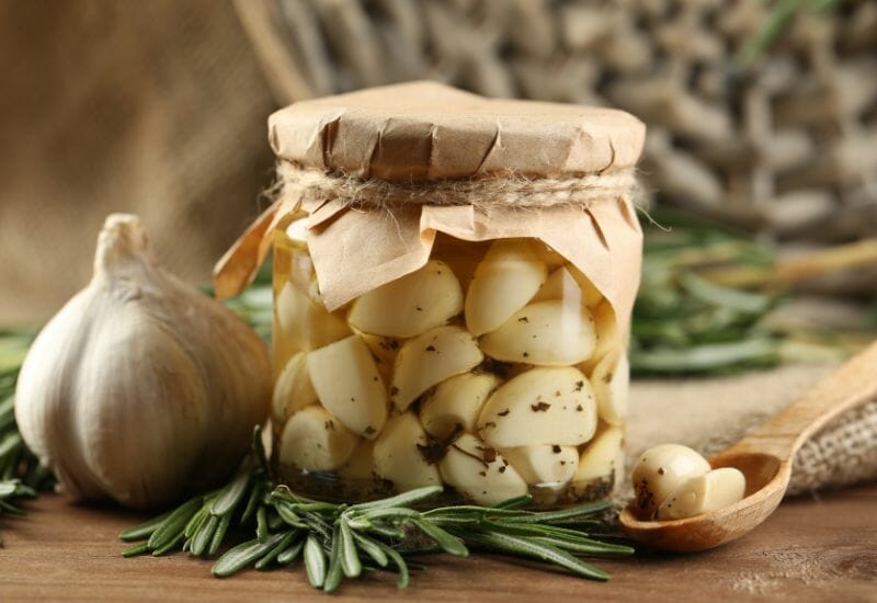 A jar of homemade pickled garlic with the top wrapped in brown paper and twine.
