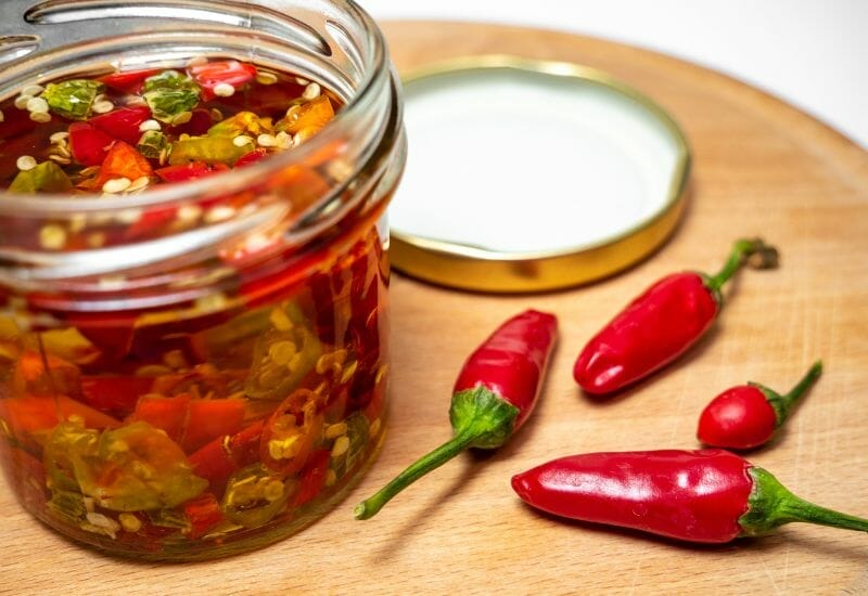 Red peppers next to a jar of pickled peppers.